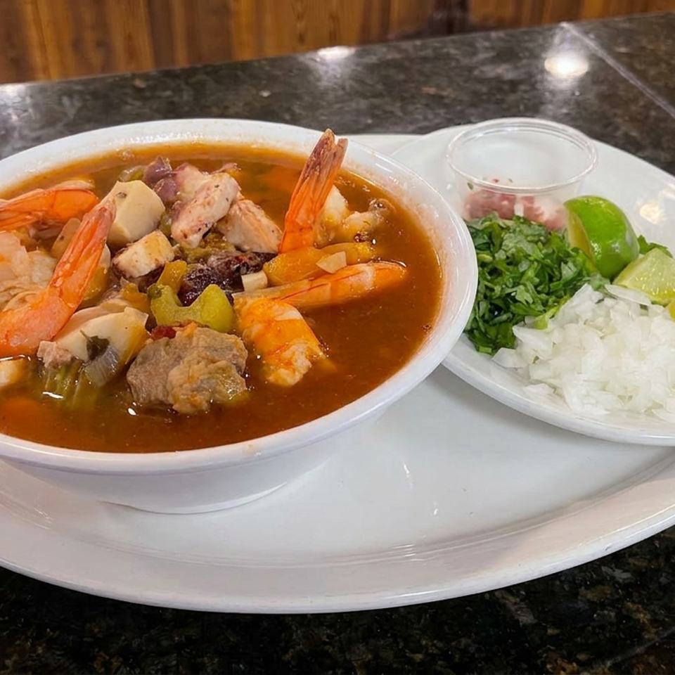 Bowl of Mexican seafood soup with shrimp, fish, and vegetables, served with lime, cilantro, chopped onion, and salsa.