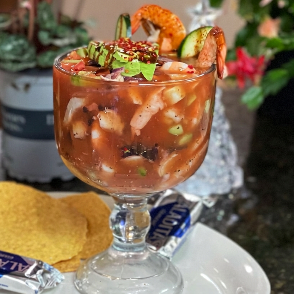 Shrimp cocktail served in a glass with cucumber, avocado, lime, and chips on a restaurant table.